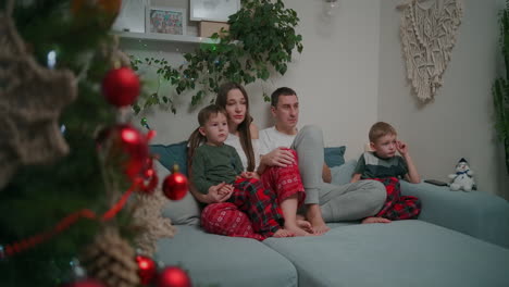 Caucasian-family-sitting-together-on-a-sofa-and-watching-TV-at-home-during-Christmas-holidays-decorated-apartment-interior.-High-quality-4k-footage